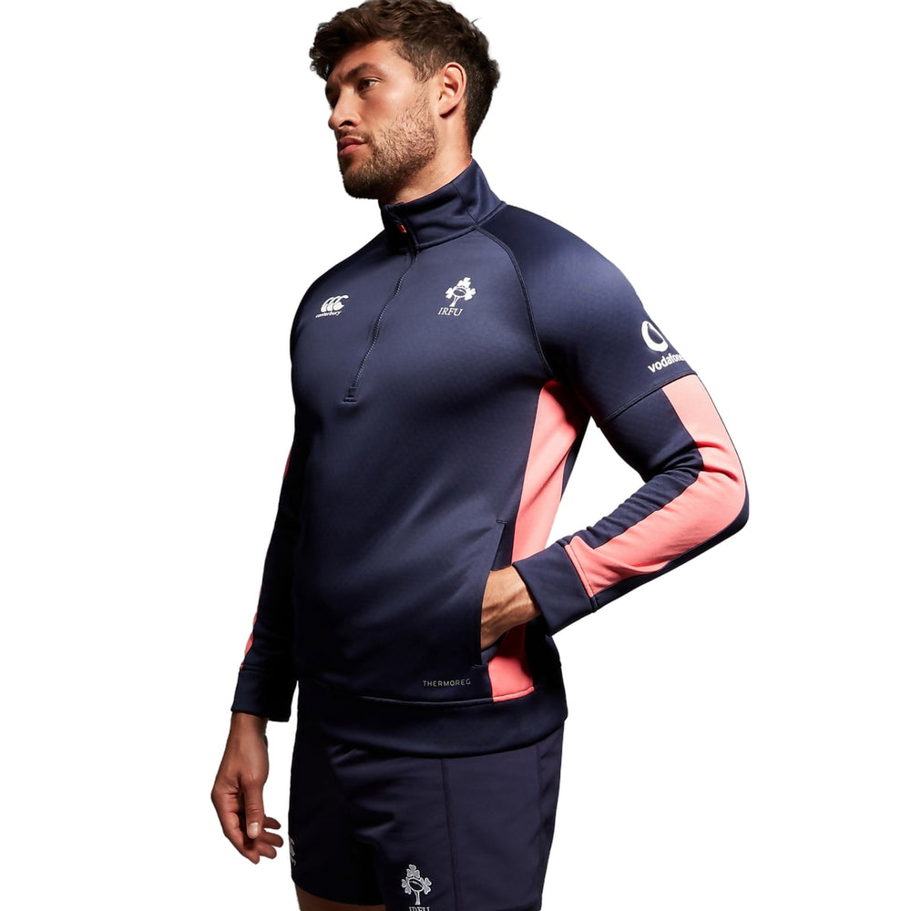 Felpa Rugby Irlanda Thermoreg 2023-24 Blu-Rosa: Maglia da allenamento da rugby irlandese blu navy e rosa con zip a un quarto, con logo della squadra e marchio dello sponsor.