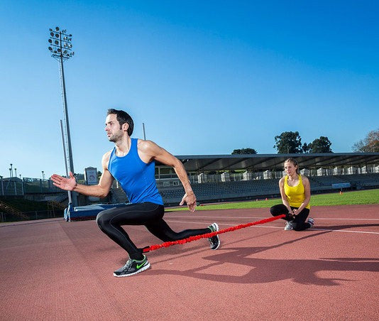 Uomo con elastico rosso per allenamento gambe in pista di atletica.