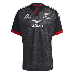 Maglia da rugby Māori All Blacks 2023-24: maglia Adidas nera con logo Maori All Blacks e intricato disegno di felci e tribù.