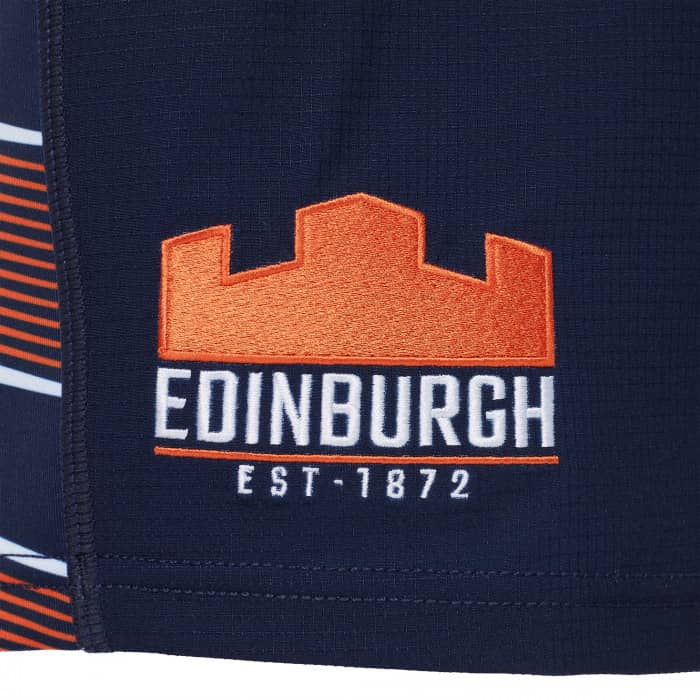 Pantaloncini Rugby Edimburgo Gara Bambino: pantaloncini da rugby per bambini blu navy con strisce arancioni e bianche, stemma di Edimburgo ricamato e scritta "EST-1872".