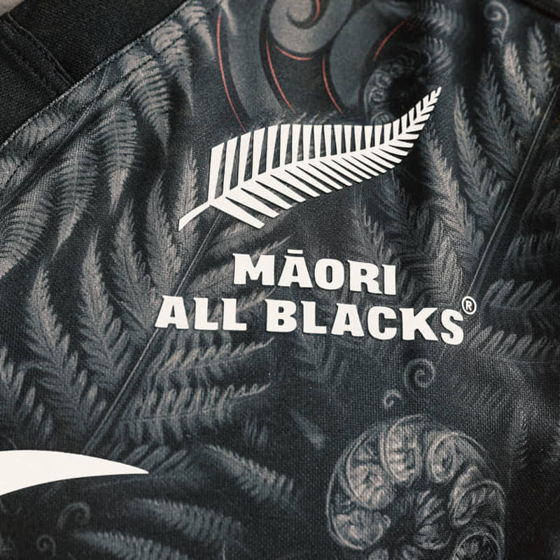 Maglia da rugby giovanile Maori All Blacks 2023-24: primo piano che mostra il logo della squadra e il motivo a felce.